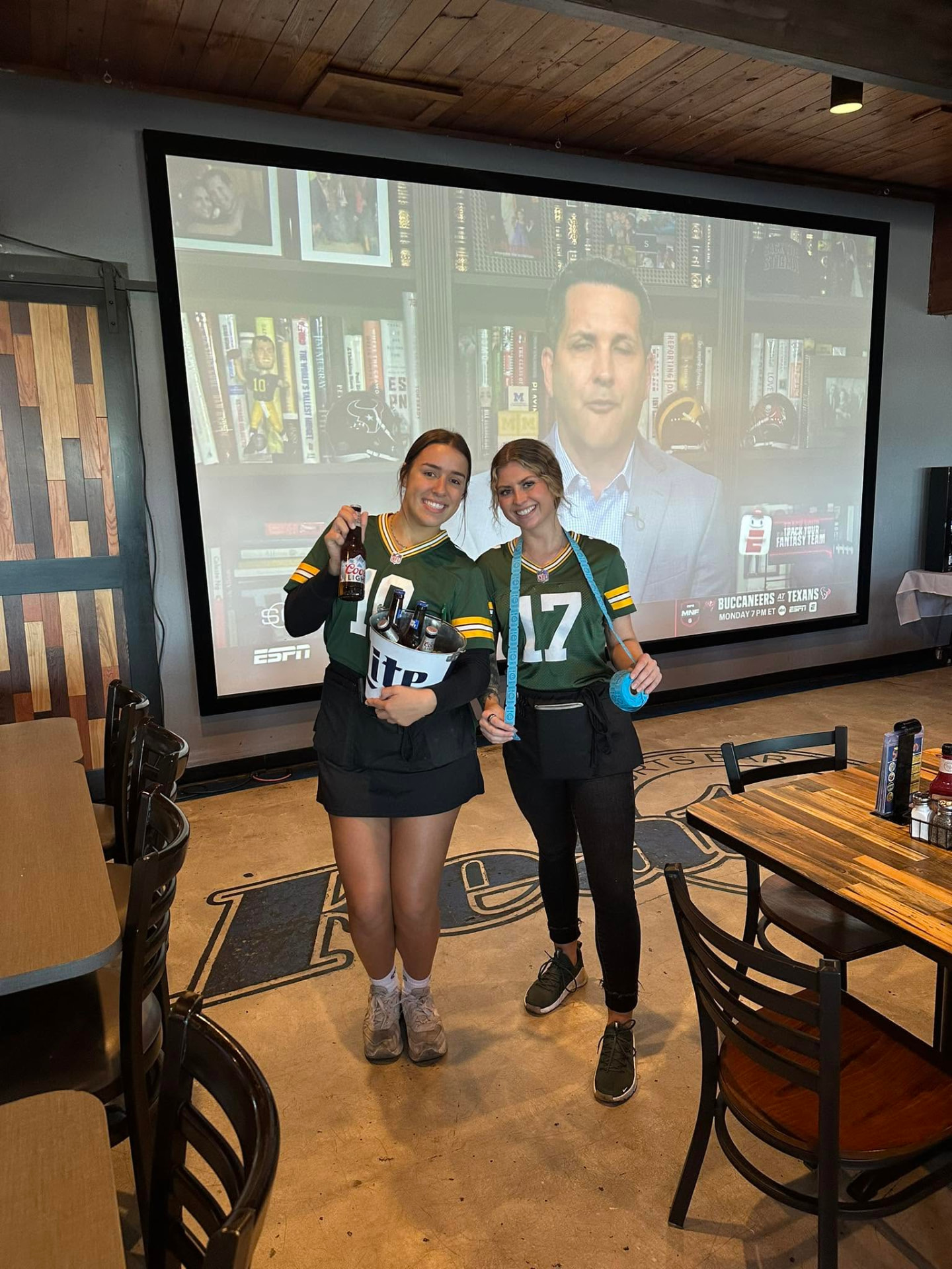 Features staff in Packers jerseys in front of the large screen